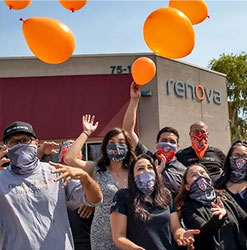 Renovians Cheering With Balloons. Group of 7 people wearing face masks celebrating in front of Renova building. There are 4 orange balloons flying up