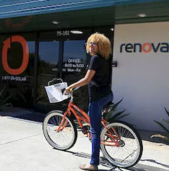Renovian Riding an orange colored bike. Woman wearing glasses on a bike parked in front of a Renova building
