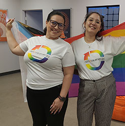 Renovians In Support Of PRIDE 2 women with white tshirts displaying renova energy with the large renova circle logo in rainbow colors. They are both smiling while holding a rainbow flag draped around their shoulders
