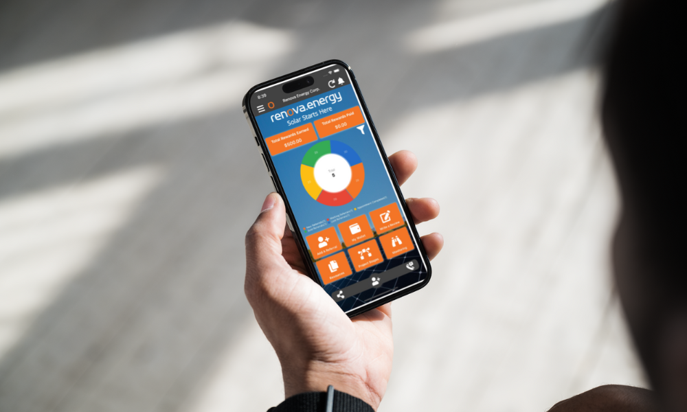 A person holds a smartphone displaying the Renva Energy app interface. The screen shows a colorful circular chart and several icons related to solar energy usage and data, amid bright natural light from a window. The view is close-up, focusing on the device in the persons hand.