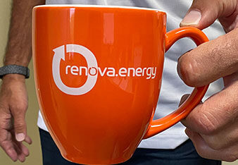 A person holds an orange mug with the renova.energy logo printed in white. The person wears a white shirt and a black wristwatch. The background is blurred, focusing on the vibrant mug and the persons hand.