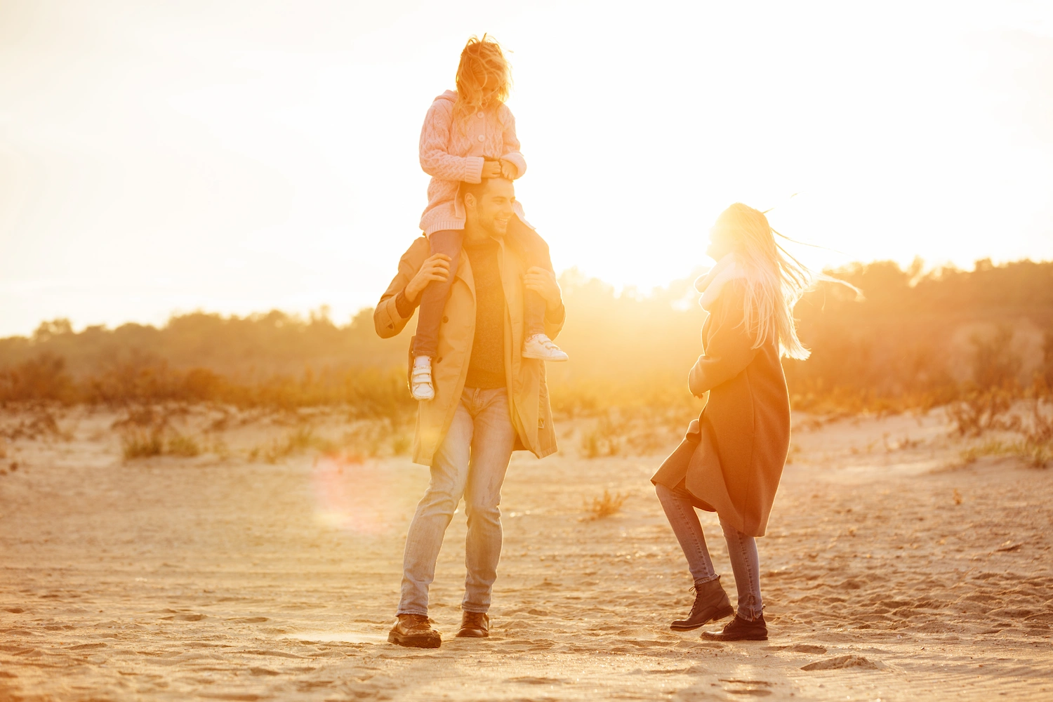 A man carries a smiling child on his shoulders while a woman stands nearby; all three appear happy, walking together beneath bright sunlight—just like families who trust Rancho Mirage Solar Panel Installers to brighten their days.