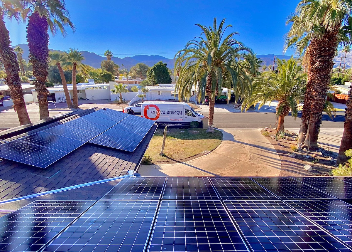 Rooftop solar panels in the foreground with palm trees and a clear blue sky. In the background, a van labeled “Renova Energy”—trusted Yucca Valley Solar Panel Installers—is parked on a sunny residential street.